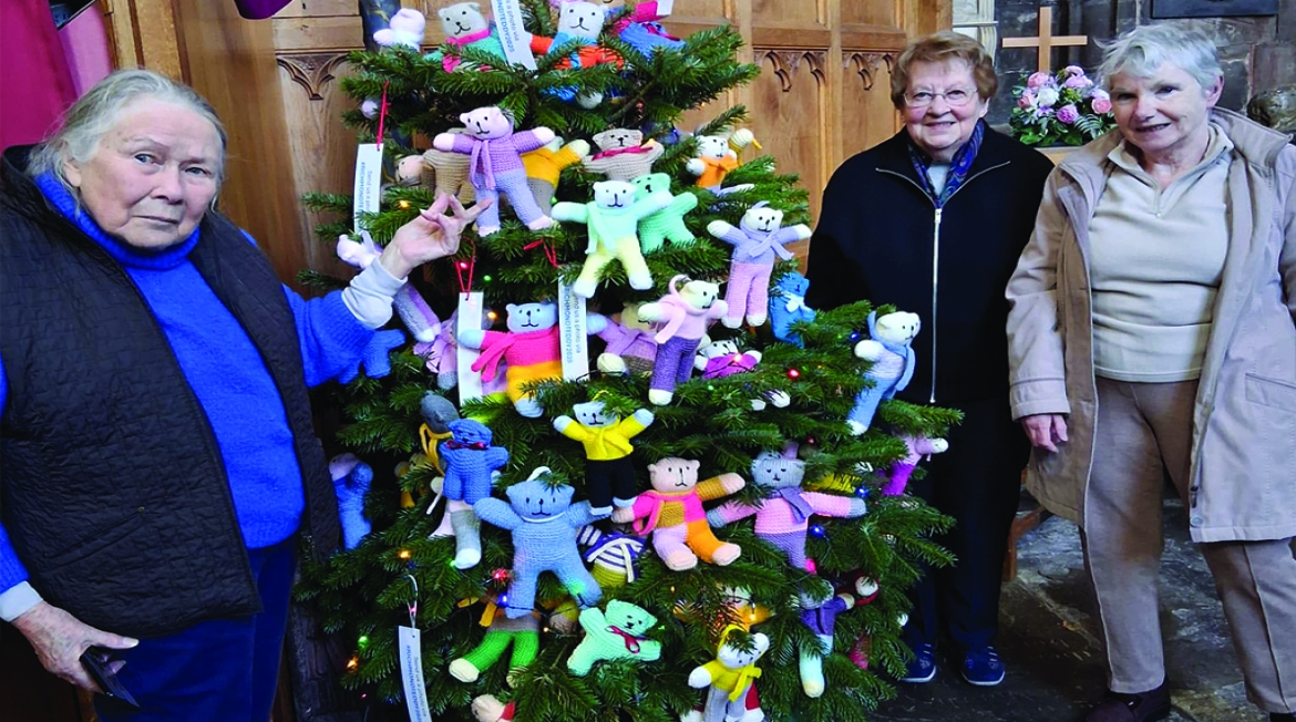Tree people standing around a Christmas tree with teddy bears