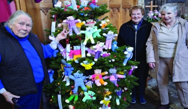 Tree people standing around a Christmas tree with teddy bears