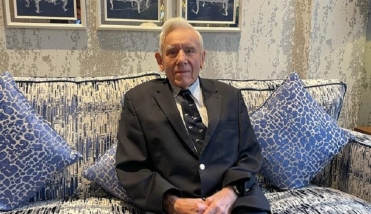 MALE RESIDENT WEARING SUIT SITS ON BLUE AND WHITE SOFA